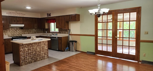 kitchen featuring under cabinet range hood, tasteful backsplash, an inviting chandelier, and dishwasher
