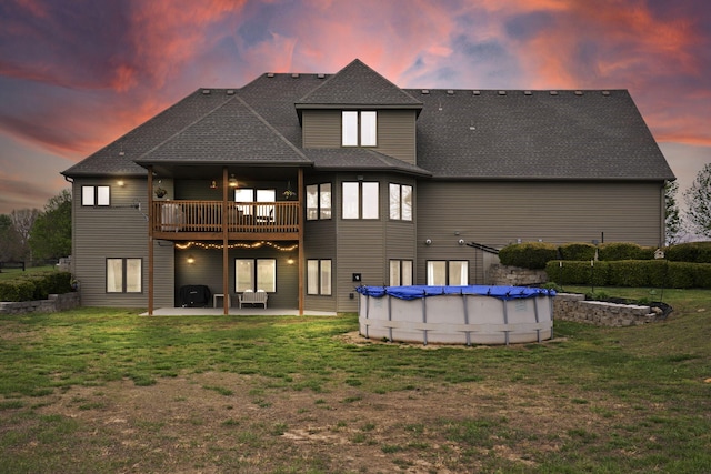 rear view of house with a wooden deck, a yard, a covered pool, a patio area, and a shingled roof
