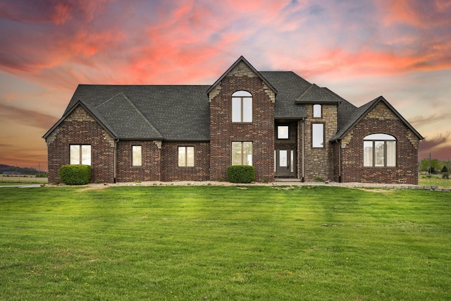 view of front of house featuring a yard, brick siding, and a shingled roof