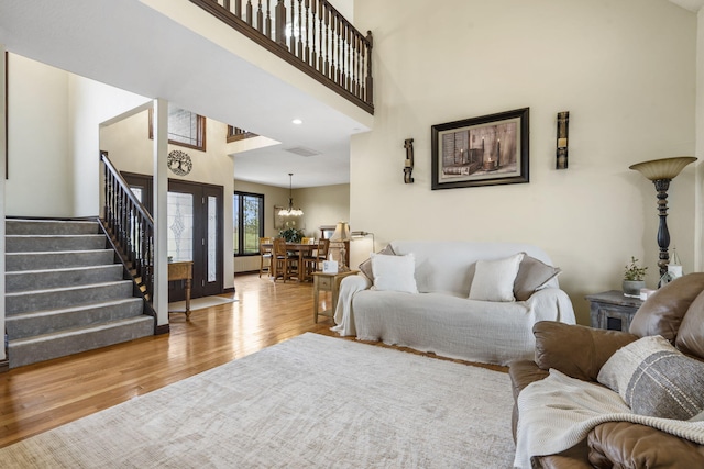 living area with an inviting chandelier, stairway, a high ceiling, visible vents, and wood finished floors