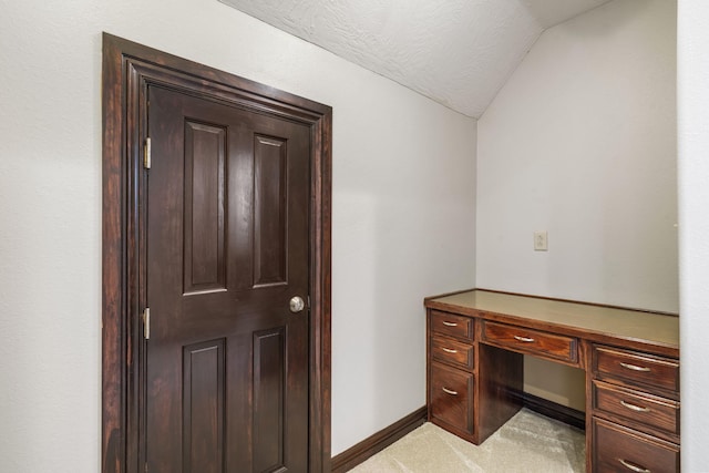 unfurnished office featuring baseboards, light colored carpet, and vaulted ceiling