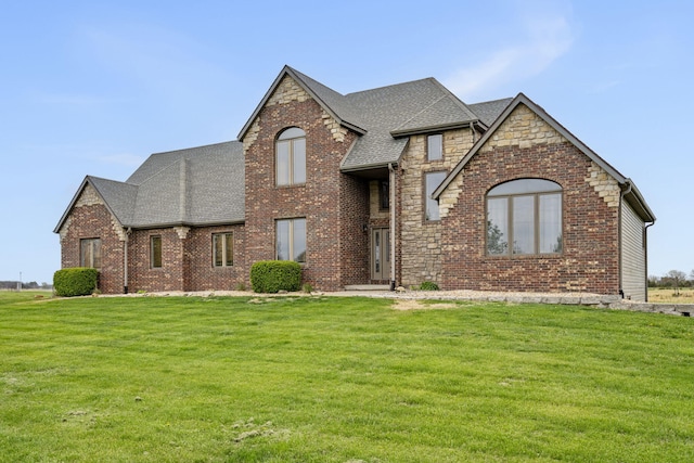view of front facade with brick siding, roof with shingles, and a front lawn