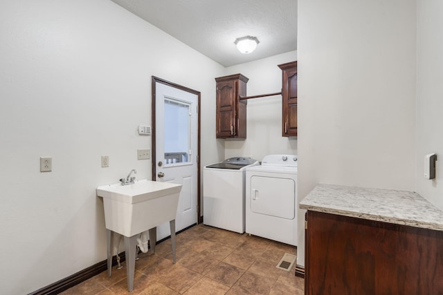 clothes washing area with a textured ceiling, visible vents, cabinet space, and washer and clothes dryer