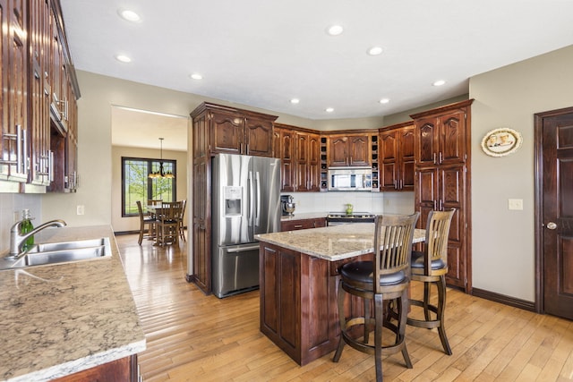 kitchen with a sink, appliances with stainless steel finishes, a kitchen bar, light wood-style floors, and backsplash
