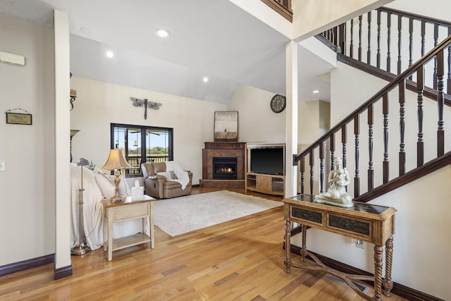 living area featuring high vaulted ceiling, stairway, a warm lit fireplace, and wood finished floors