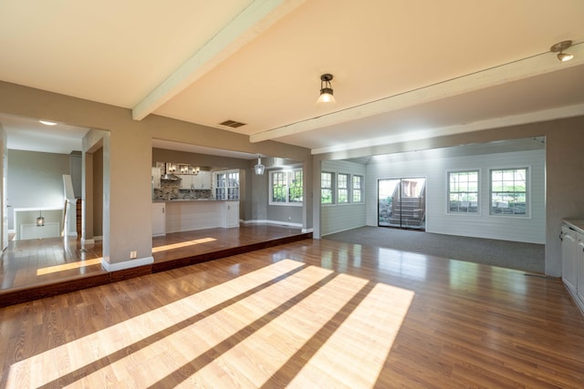 unfurnished living room with a wealth of natural light, baseboards, wood finished floors, and beam ceiling