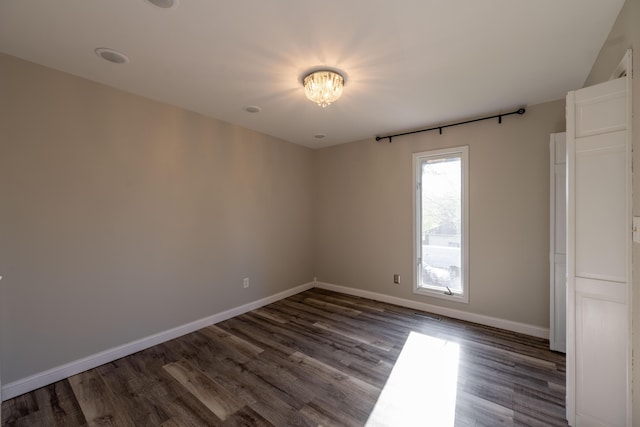 empty room featuring dark wood finished floors, baseboards, and an inviting chandelier