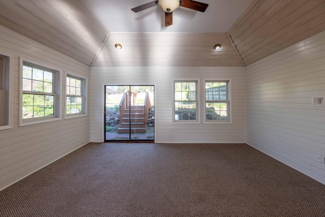 carpeted spare room with wooden walls, vaulted ceiling, and ceiling fan