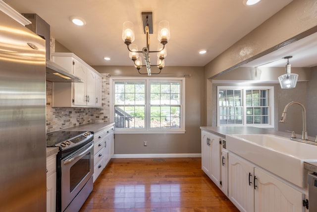 kitchen featuring a sink, wood-type flooring, decorative light fixtures, appliances with stainless steel finishes, and white cabinetry