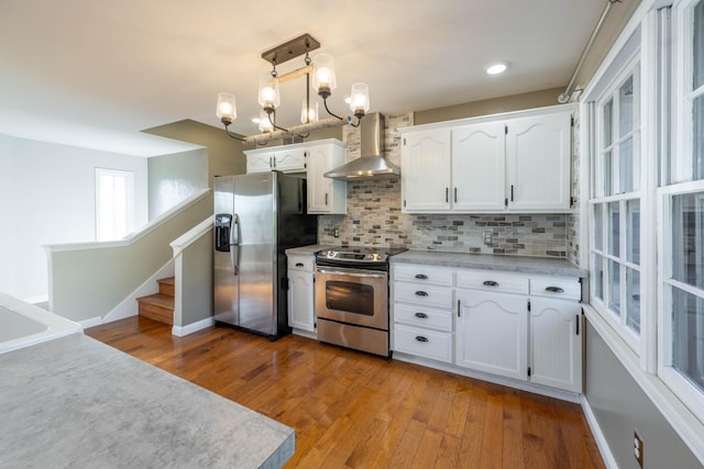kitchen featuring white cabinets, light wood finished floors, backsplash, wall chimney range hood, and appliances with stainless steel finishes