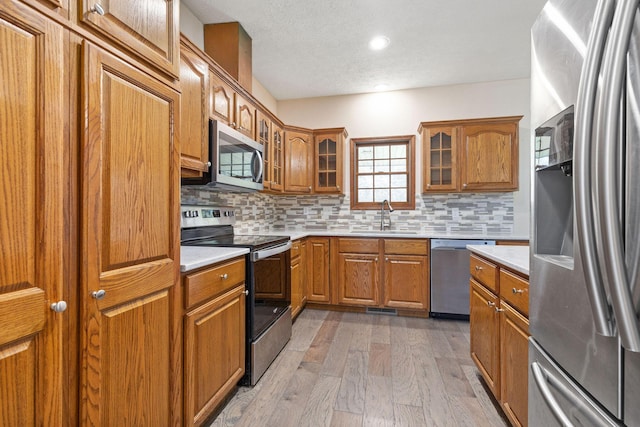 170 Oakridge Ave, Branson, MO 65616 - kitchen with appliances with stainless steel finishes, a sink, brown cabinetry, tasteful backsplash, and a textured ceiling