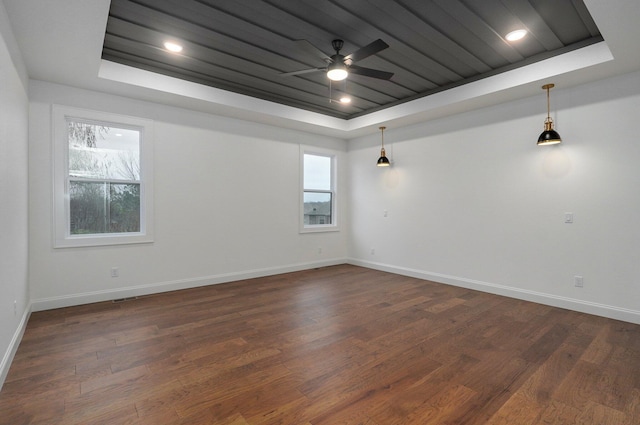 spare room featuring dark wood finished floors, a raised ceiling, a ceiling fan, and baseboards