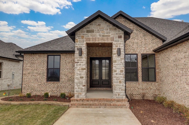entrance to property with stone siding, roof with shingles, and brick siding