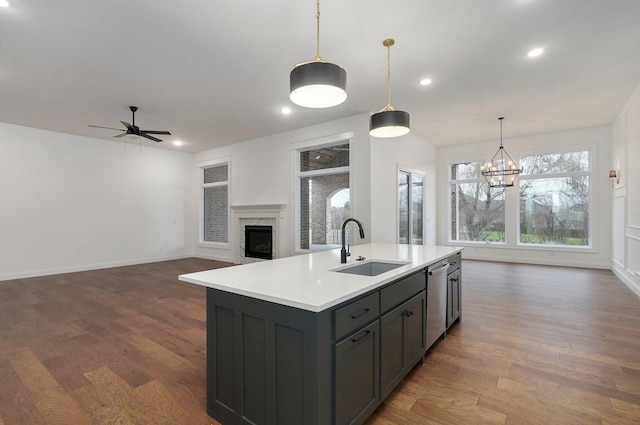 kitchen with light countertops, stainless steel dishwasher, a sink, a kitchen island with sink, and a fireplace