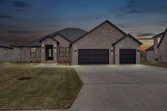 french country home with a lawn, concrete driveway, brick siding, and a garage