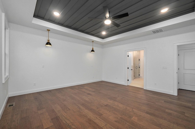 empty room with a tray ceiling, visible vents, dark wood-type flooring, and ceiling fan