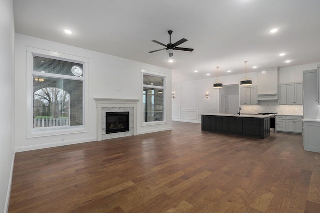unfurnished living room featuring recessed lighting, a ceiling fan, a sink, a premium fireplace, and dark wood-style flooring
