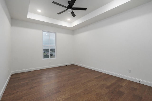 unfurnished room featuring baseboards, dark wood-style floors, ceiling fan, and a tray ceiling
