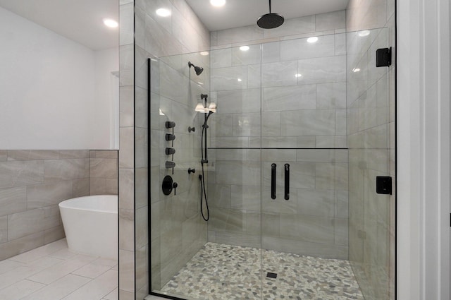 full bath featuring tile walls, a freestanding tub, tile patterned flooring, and a stall shower