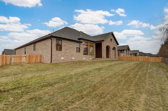 rear view of property with a lawn, a fenced backyard, and brick siding