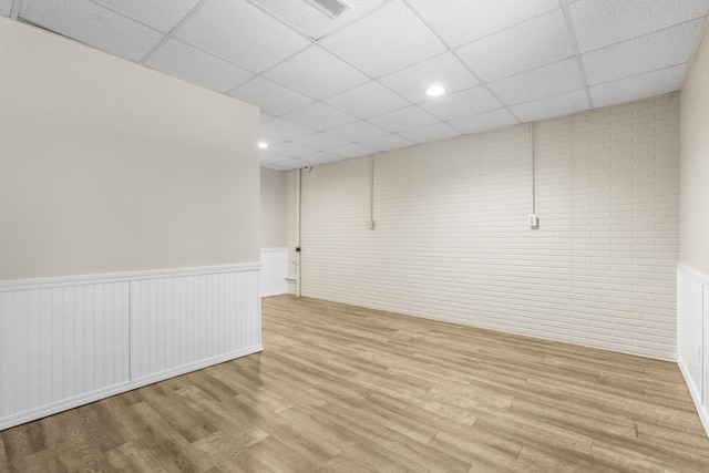 finished basement featuring wood finished floors, visible vents, a drop ceiling, and a wainscoted wall