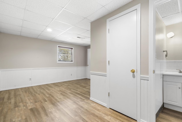 interior space featuring light wood-style floors, a paneled ceiling, a sink, and wainscoting