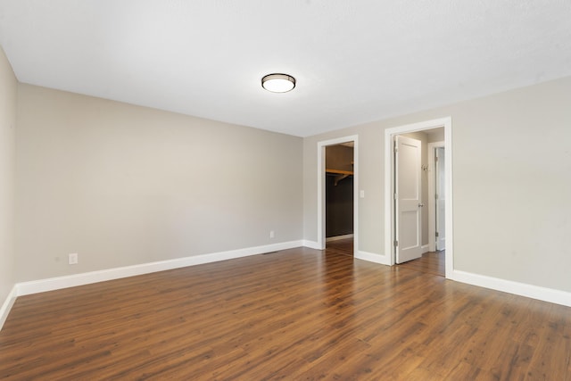 interior space featuring a walk in closet, a closet, baseboards, and dark wood-style flooring