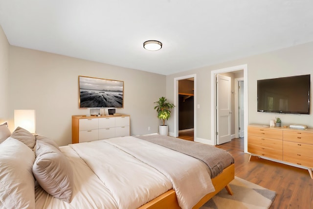 bedroom with a walk in closet and wood finished floors