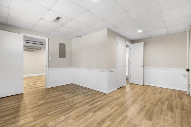 basement featuring wood finished floors, wainscoting, a paneled ceiling, and visible vents