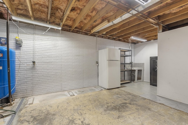 unfinished basement featuring brick wall and freestanding refrigerator