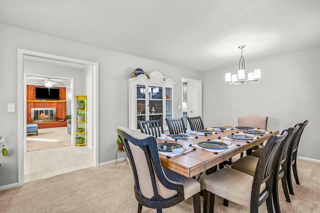 dining space with a brick fireplace, baseboards, an inviting chandelier, and light carpet