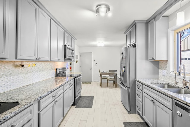 kitchen featuring light wood-style floors, gray cabinets, tasteful backsplash, a sink, and stainless steel appliances