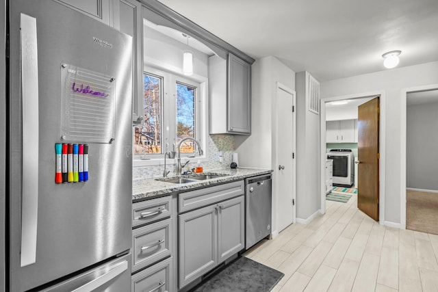 kitchen featuring light stone countertops, baseboards, a sink, gray cabinetry, and stainless steel appliances