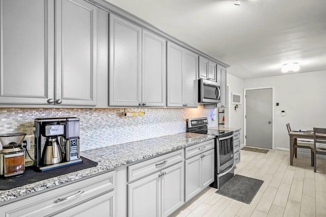 kitchen with light stone countertops, baseboards, backsplash, gray cabinetry, and stainless steel appliances