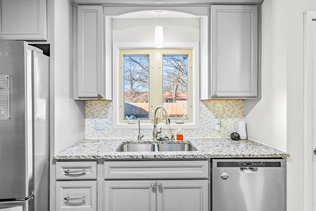 kitchen with light stone counters, a sink, appliances with stainless steel finishes, and tasteful backsplash