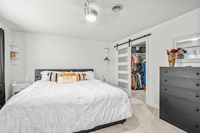 bedroom with a textured ceiling, visible vents, light colored carpet, a barn door, and a spacious closet