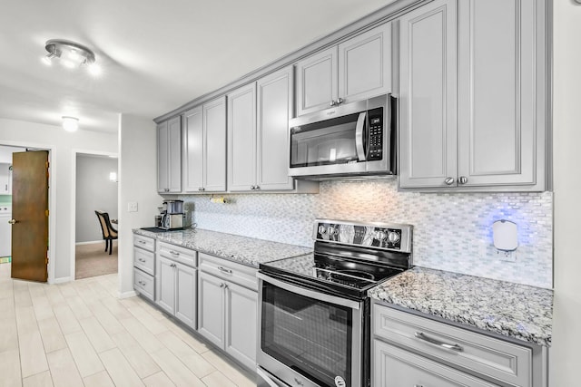 kitchen featuring stainless steel appliances, baseboards, gray cabinets, and tasteful backsplash