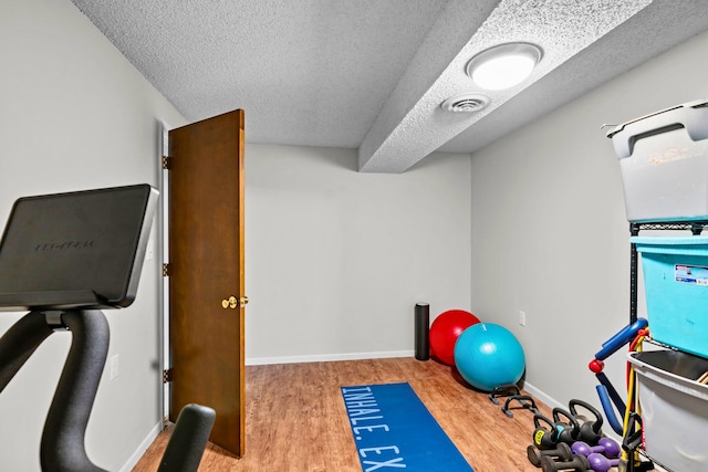 workout room featuring baseboards, visible vents, a textured ceiling, and wood finished floors