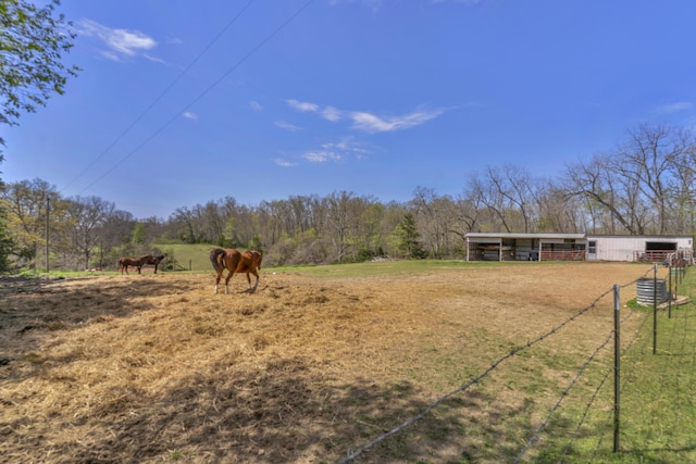 view of yard featuring a rural view, an exterior structure, an outbuilding, and fence