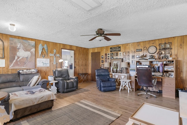living room with ceiling fan, wood finished floors, a textured ceiling, and wooden walls