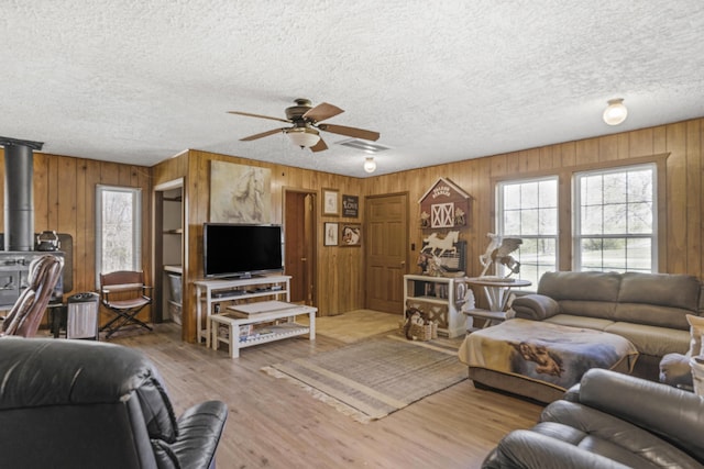 living room featuring wood finished floors, a wood stove, wood walls, and ceiling fan