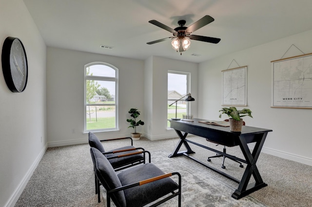 office space featuring light colored carpet, ceiling fan, baseboards, and a healthy amount of sunlight
