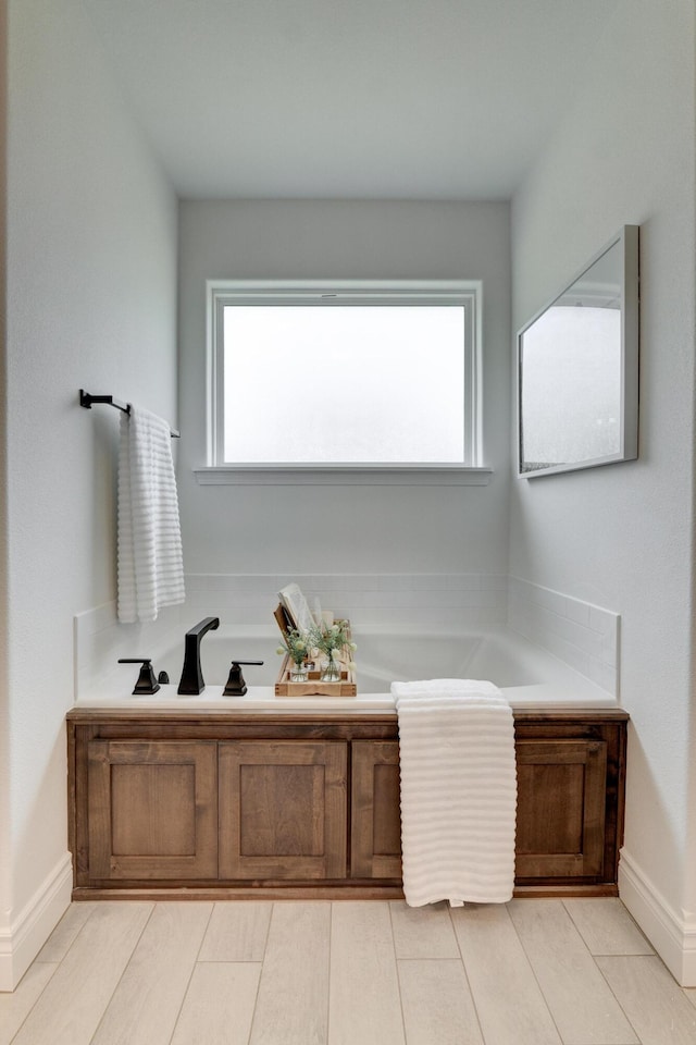 bathroom featuring a bath, plenty of natural light, and baseboards