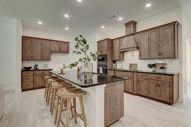 kitchen with a kitchen island with sink, a sink, tasteful backsplash, custom range hood, and black appliances