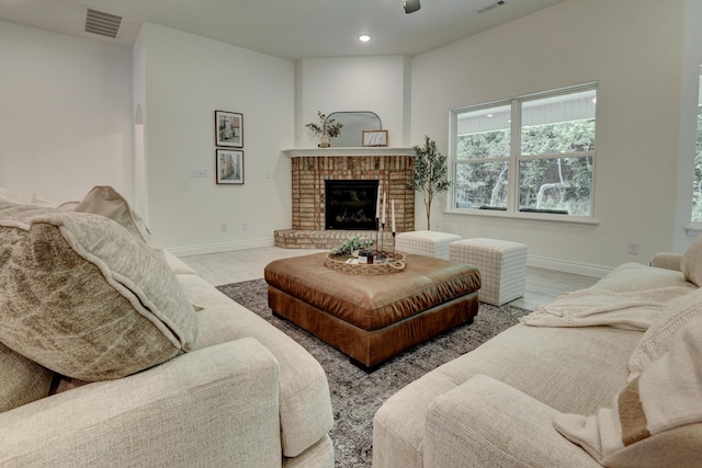 living area featuring wood finished floors, baseboards, a brick fireplace, visible vents, and recessed lighting