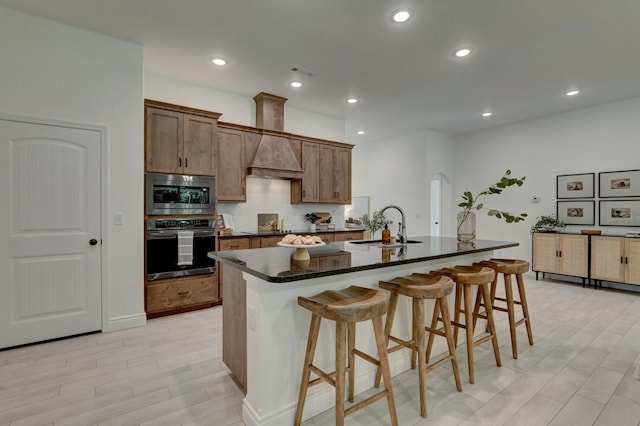 kitchen with a kitchen island with sink, a kitchen breakfast bar, a sink, custom exhaust hood, and appliances with stainless steel finishes