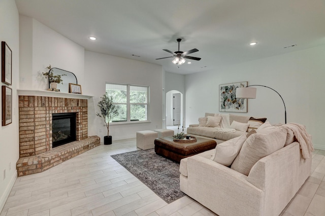 living area featuring arched walkways, a brick fireplace, baseboards, and ceiling fan