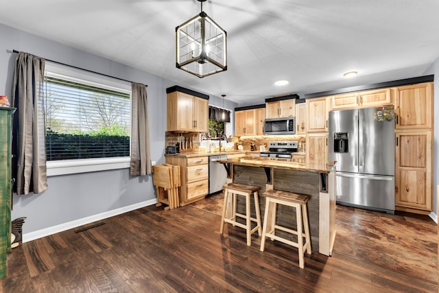 kitchen featuring light brown cabinets, appliances with stainless steel finishes, a breakfast bar, and dark wood-style floors