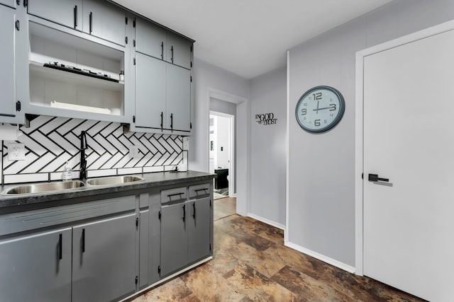 kitchen featuring a sink, tasteful backsplash, dark countertops, baseboards, and stone finish flooring
