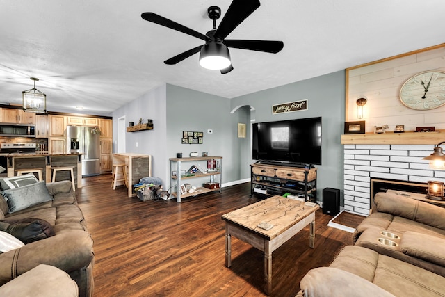 living room with arched walkways, dark wood-style floors, a fireplace, and ceiling fan